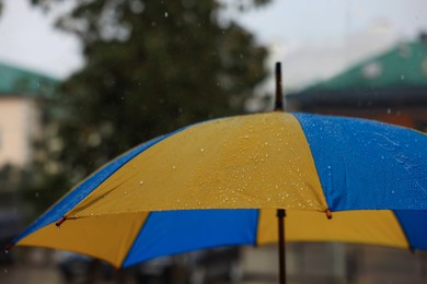 Photo of Yellow and blue umbrella outdoors on rainy day, closeup