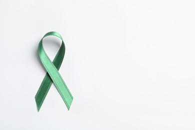 Green ribbon on white background, top view. Cancer awareness