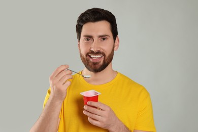 Handsome man with delicious yogurt and spoon on light grey background