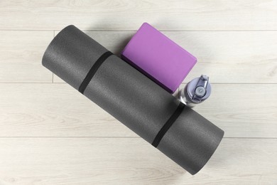 Photo of Exercise mat, yoga block and bottle of water on light wooden floor, flat lay