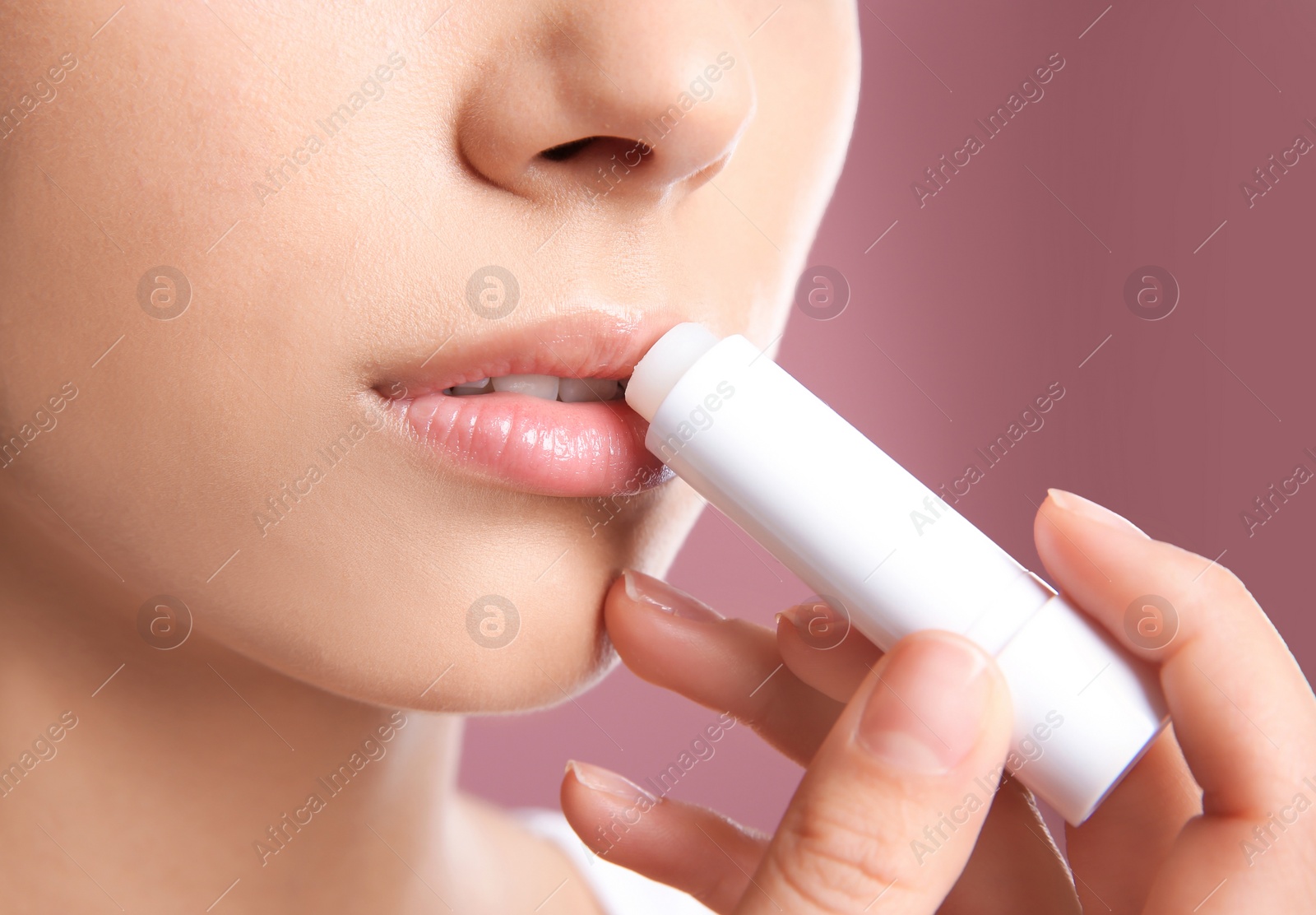 Photo of Young woman applying balm on her lips against color background, closeup