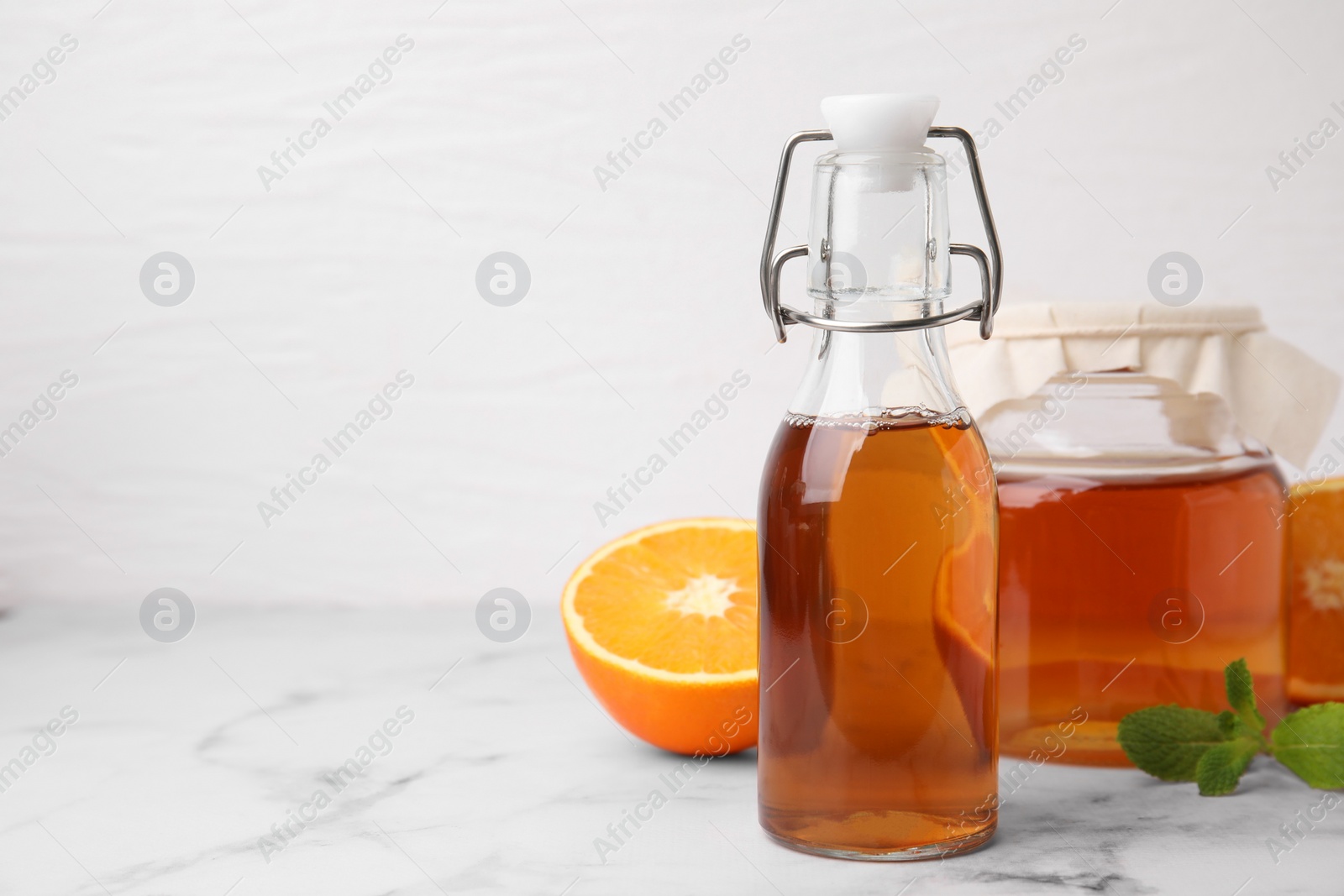 Photo of Tasty kombucha, orange and mint on white marble table, space for text