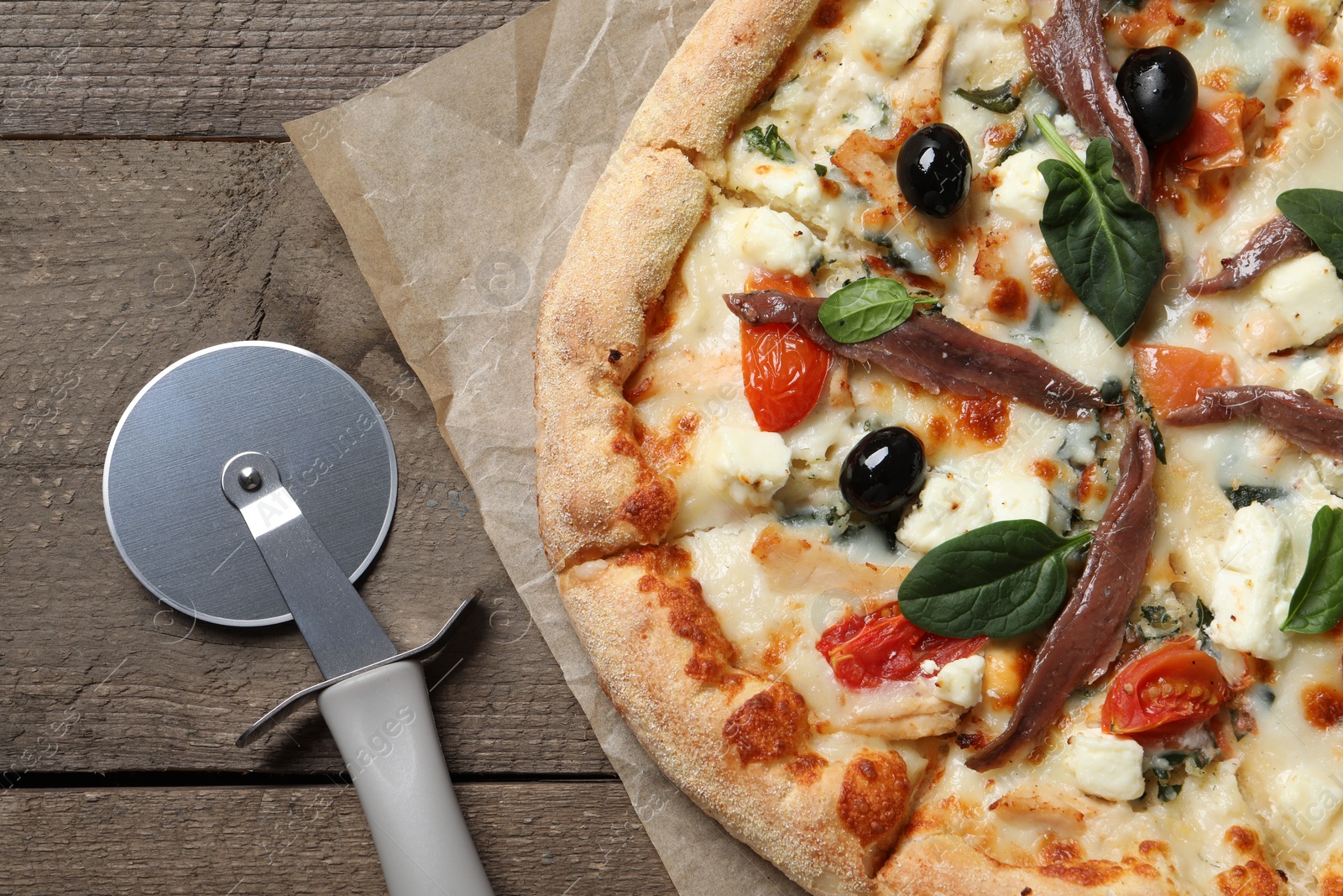 Photo of Tasty pizza with anchovies and cutter on wooden table, top view