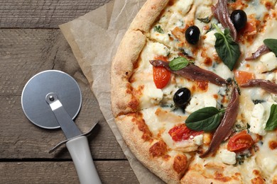 Tasty pizza with anchovies and cutter on wooden table, top view