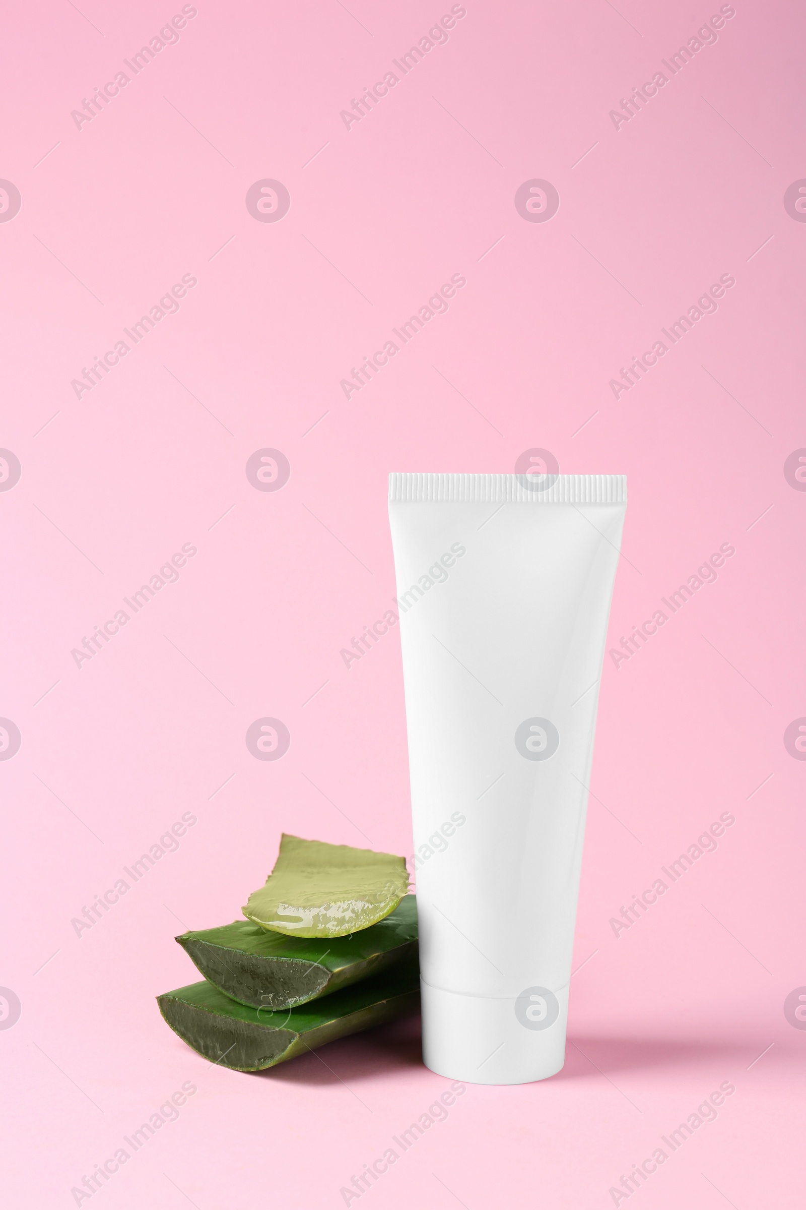 Photo of Tube of natural cream and cut aloe on pink background