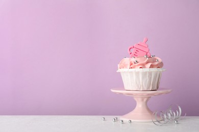 Photo of Baby shower cupcake with pink cream and topper on white table against violet background, space for text