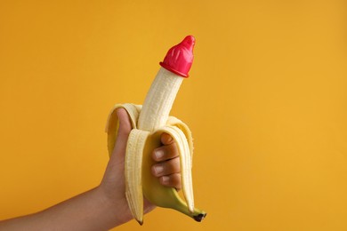 Photo of Woman holding banana in condom on orange background, closeup and space for text. Safe sex concept