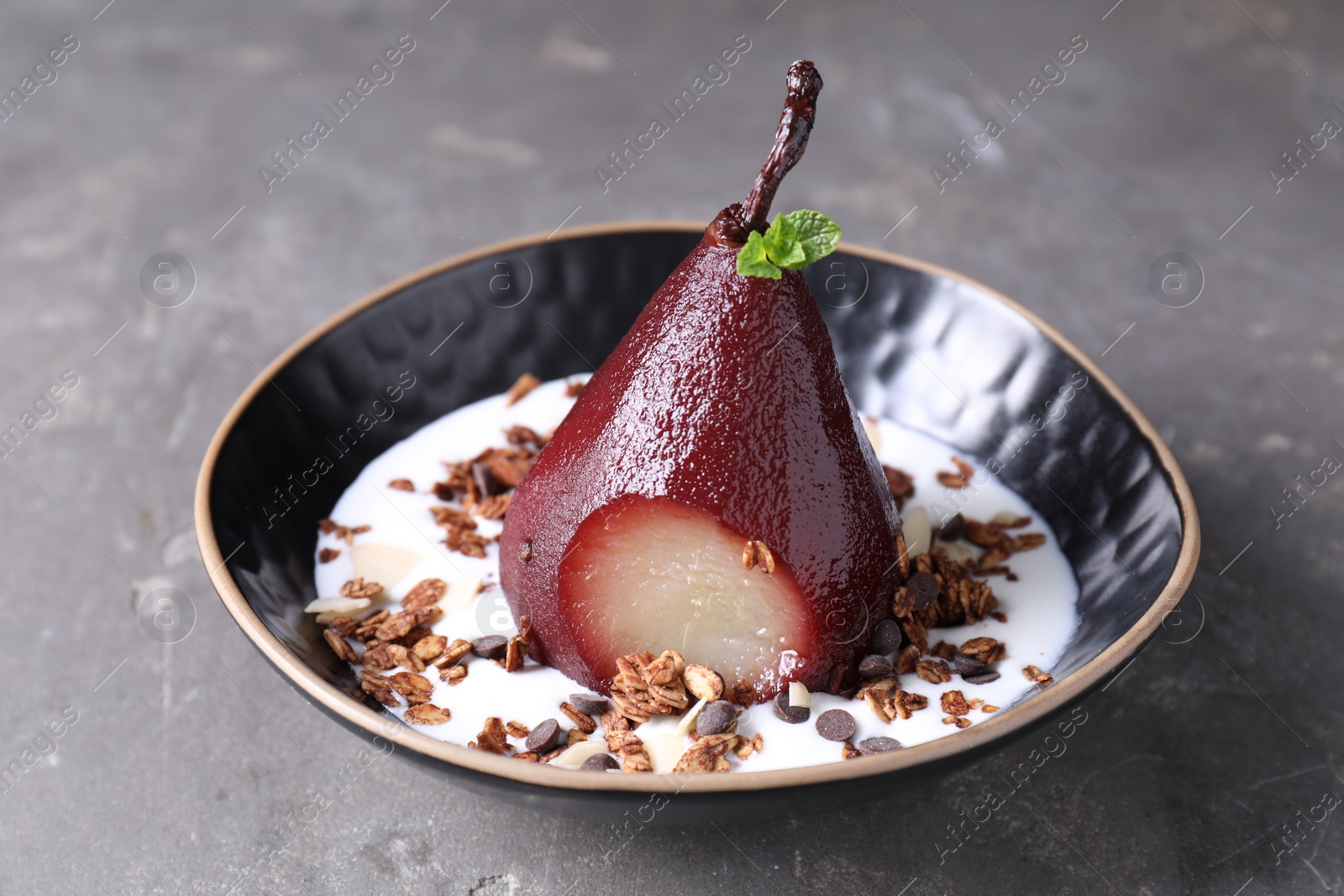 Photo of Tasty red wine poached pear with muesli and yoghurt in bowl on grey table, closeup