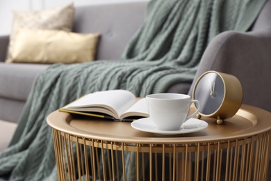 Photo of Coffee table with cup of tea, clock and book near sofa in room