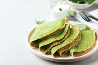 Tasty spinach crepes on light grey table, closeup