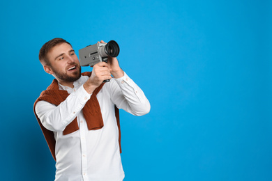 Young man with vintage video camera on light blue background, space for text