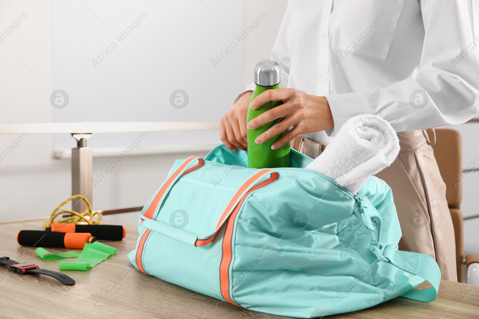 Photo of Businesswoman packing sports stuff for training into bag in office, closeup