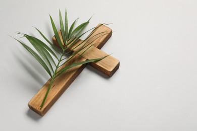 Photo of Wooden cross and palm leaf on light grey background, space for text. Easter attributes