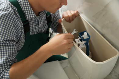 Photo of Professional plumber repairing toilet in bathroom, closeup