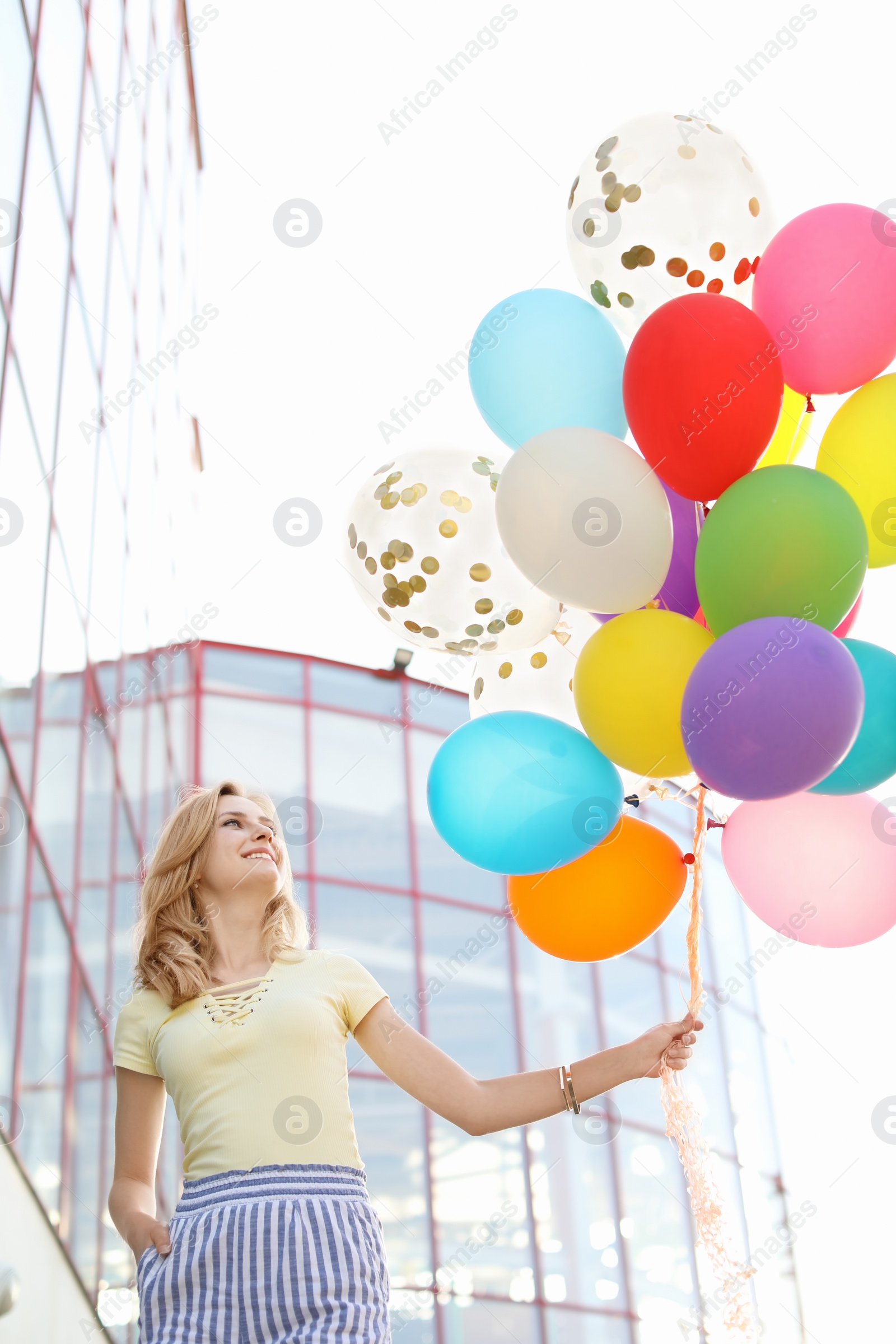 Photo of Young woman with colorful balloons outdoors on sunny day