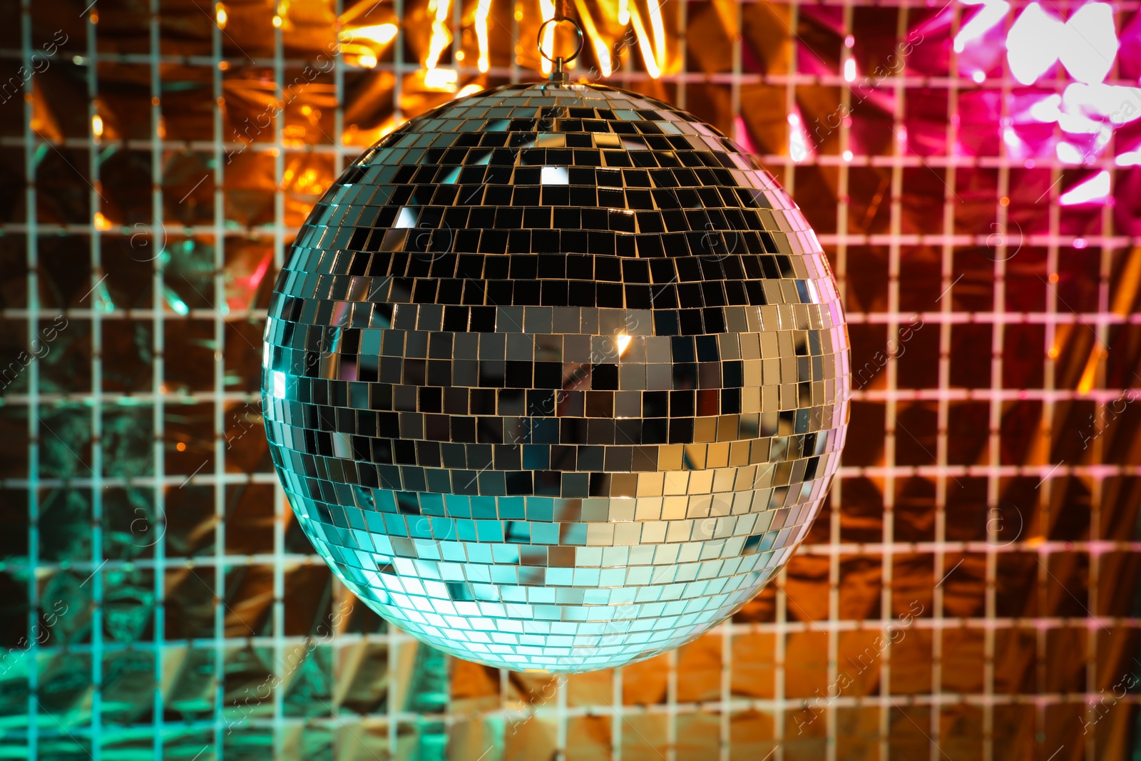 Photo of Shiny disco ball against foil party curtain under turquoise and orange light