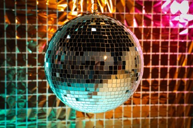 Photo of Shiny disco ball against foil party curtain under turquoise and orange light