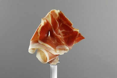 Photo of Fork with slice of tasty jamon on light grey background, closeup