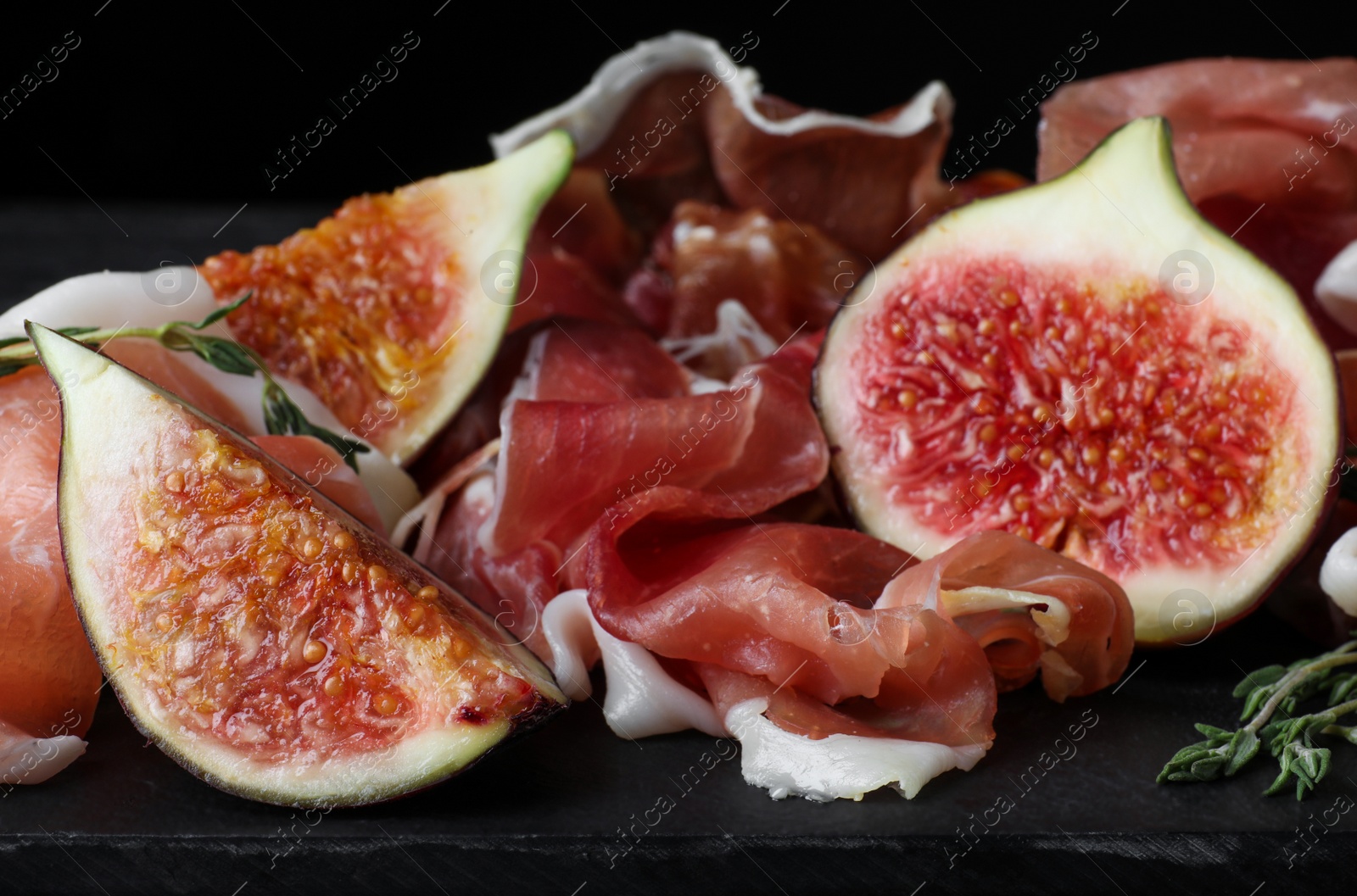 Photo of Delicious ripe figs and prosciutto served on slate board, closeup