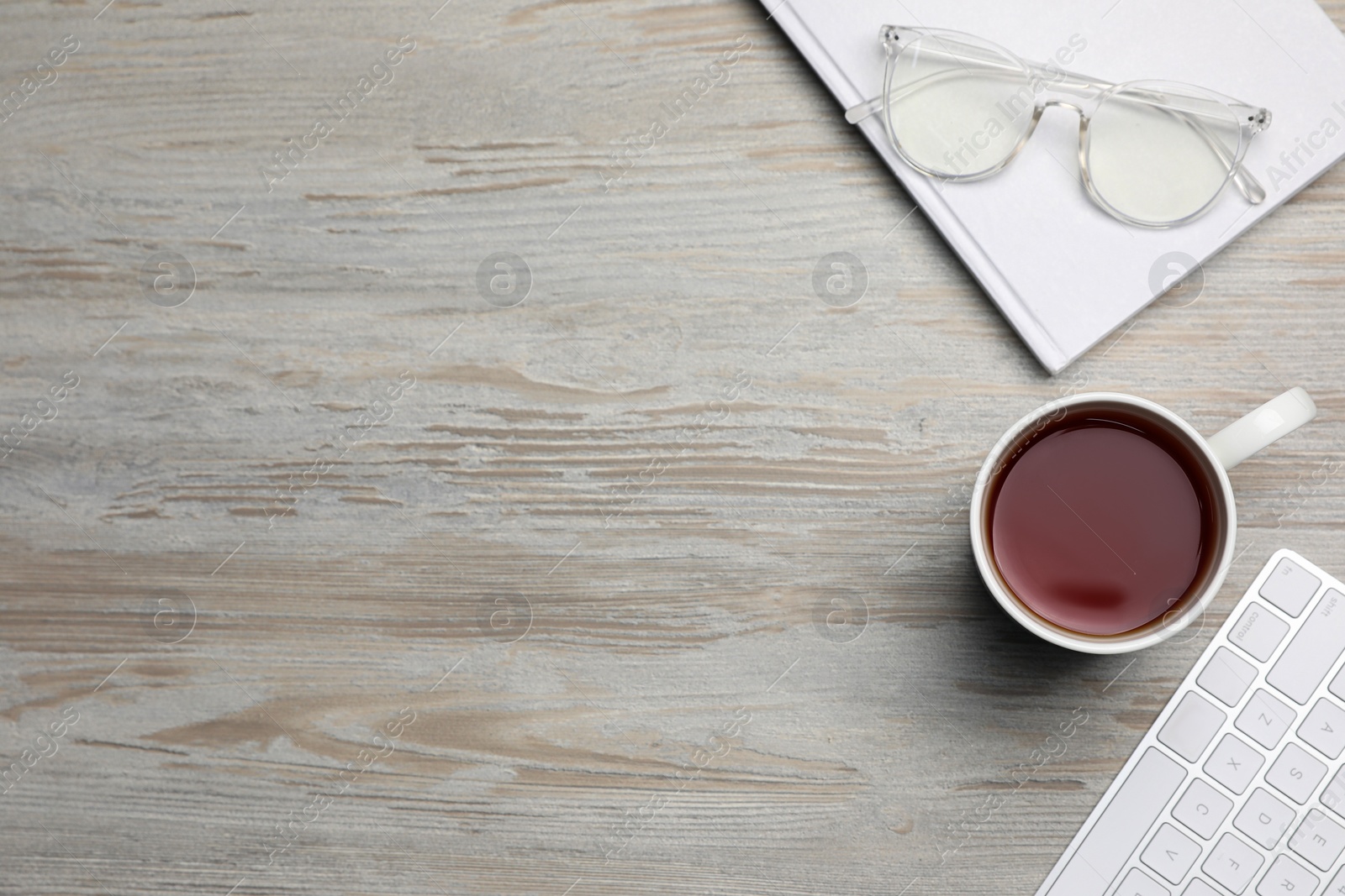 Ceramic mug of aromatic tea, keyboard, book and glasses on white wooden table, flat lay. Space for text Photo of Ceramic mug of aromatic tea, keyboard, book and glasses on white wooden table, flat lay. Space for text