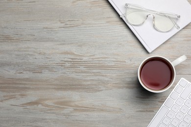 Photo of Ceramic mug of aromatic tea, keyboard, book and glasses on white wooden table, flat lay. Space for text