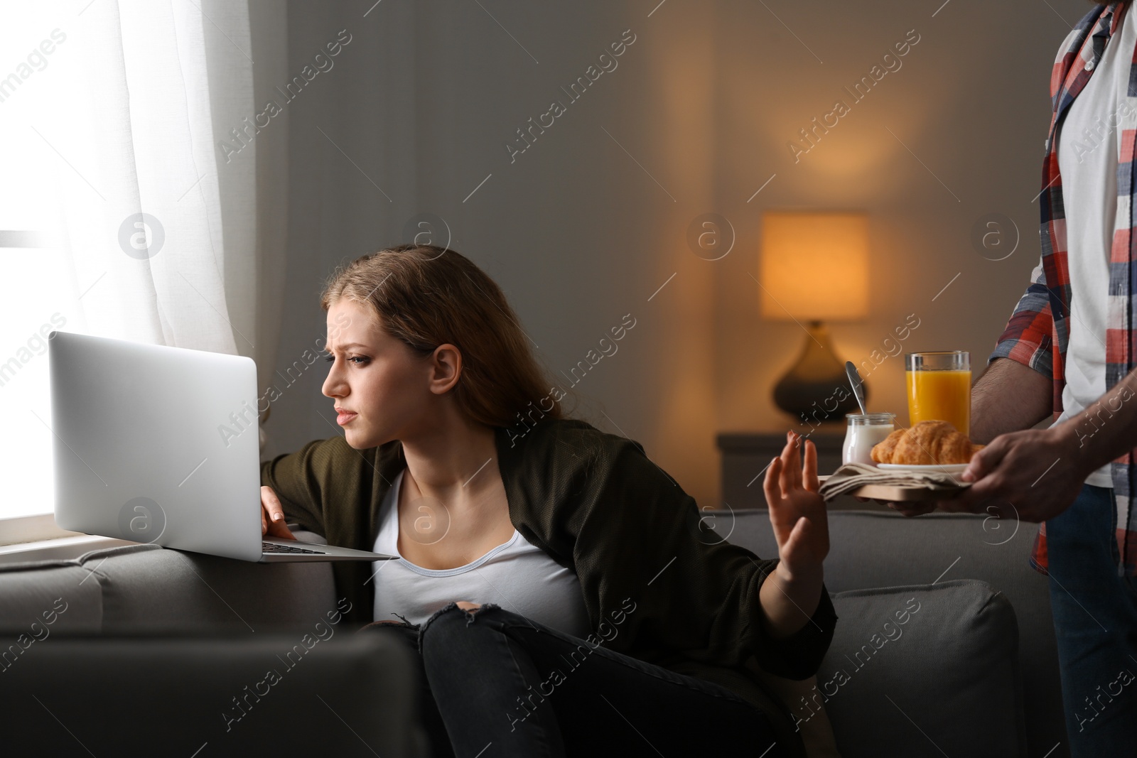 Photo of Young woman with laptop ignoring her boyfriend at home. Loneliness concept