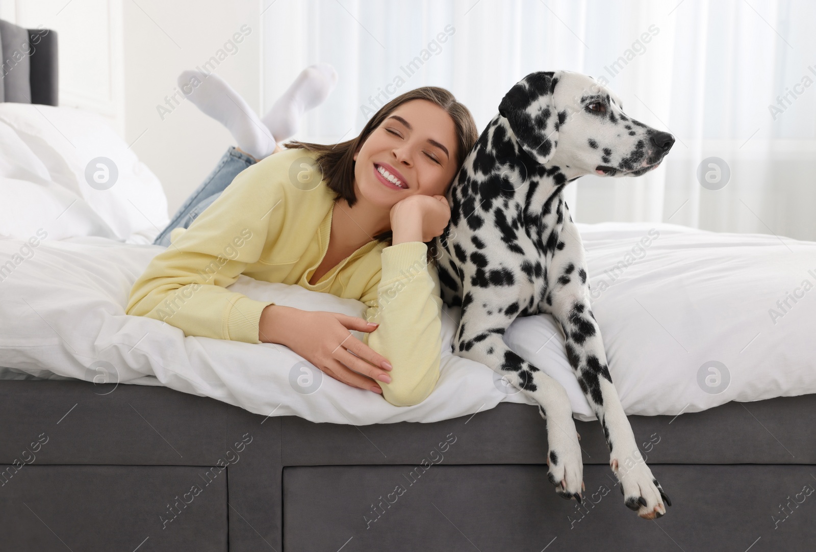 Photo of Beautiful woman with her adorable Dalmatian dog on bed at home. Lovely pet