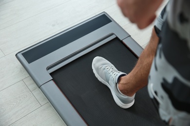 Photo of Sporty man training on walking treadmill at home, closeup