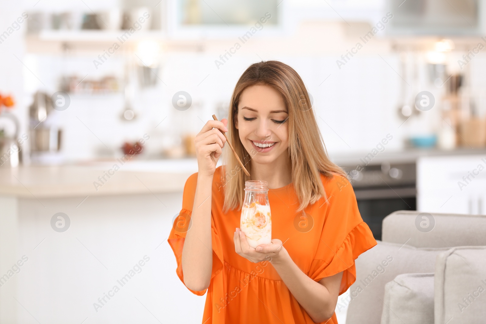 Photo of Young attractive woman eating tasty yogurt in kitchen