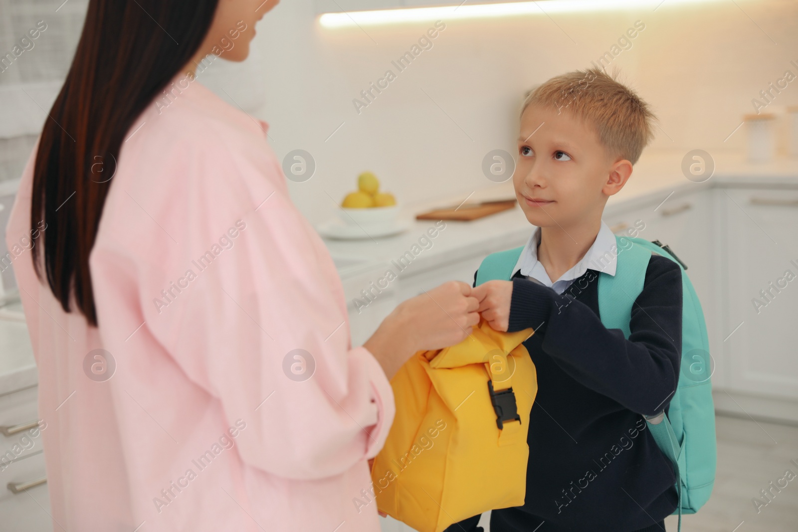 Photo of Young mother helping her little child get ready for school in kitchen, closeup