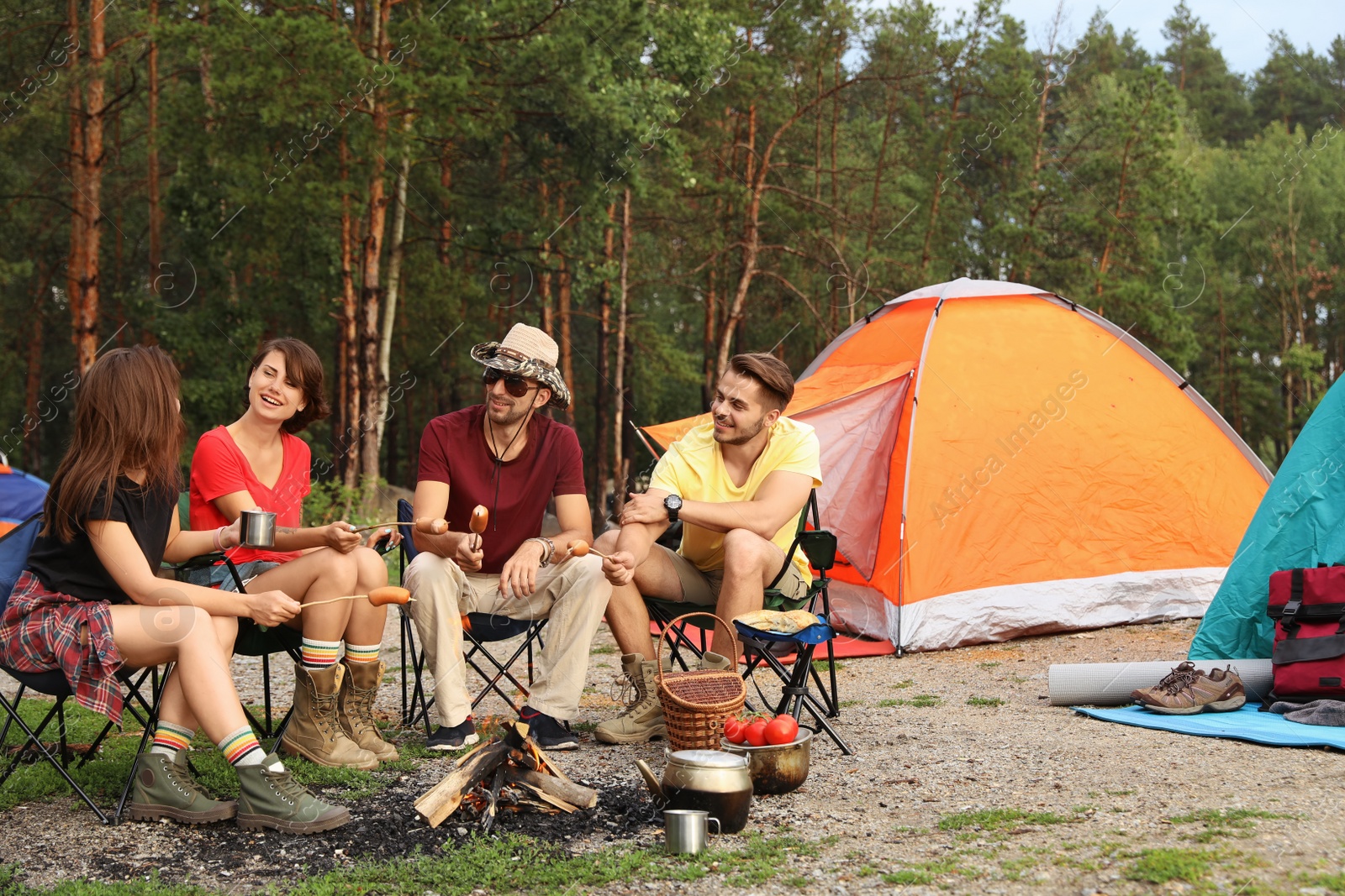 Photo of People having lunch with sausages near camping tent outdoors