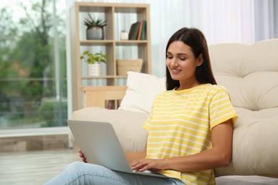 Photo of Young woman working with laptop near sofa at home