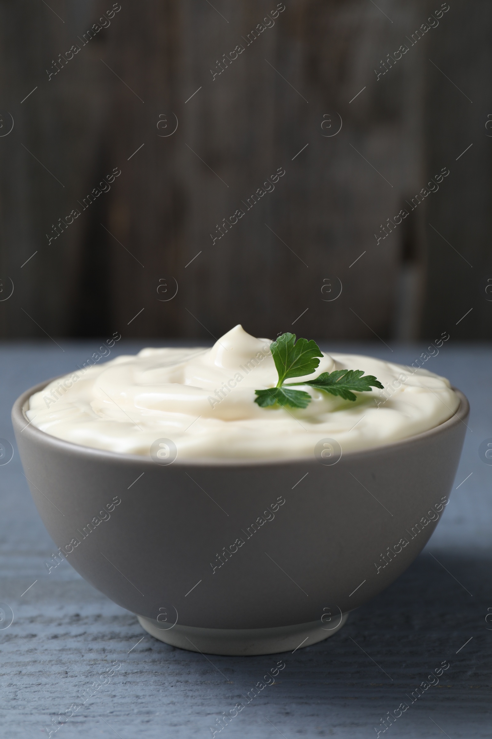 Photo of Tasty mayonnaise and parsley in bowl on gray wooden table, closeup. Space for text