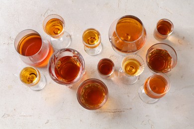 Different delicious liqueurs in glasses on light grey table, flat lay