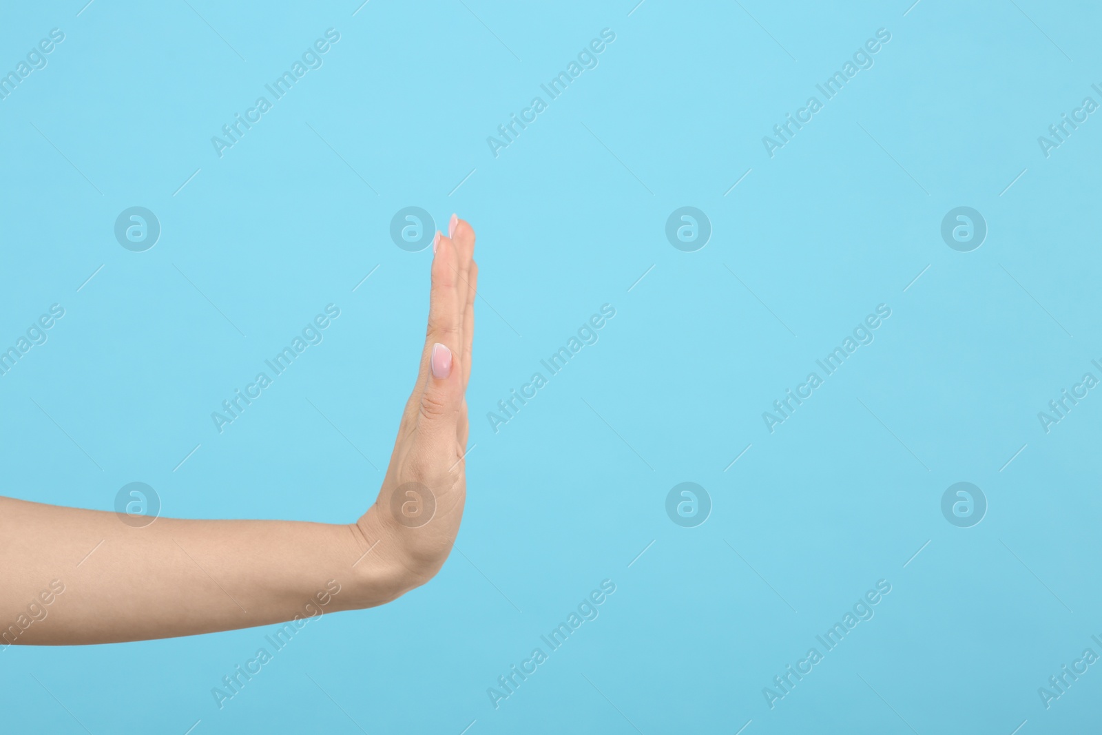 Photo of Woman showing stop gesture on light blue background, closeup. Space for text