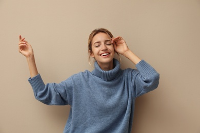 Photo of Beautiful young woman wearing knitted sweater on beige background