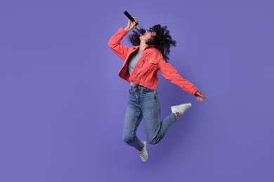 Photo of Beautiful young woman with microphone singing and jumping on purple background