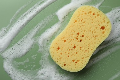 Yellow sponge with foam on green background, top view