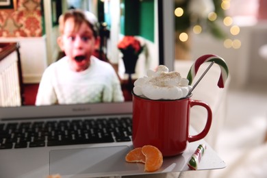 Photo of MYKOLAIV, UKRAINE - DECEMBER 25, 2020: Laptop displaying Home Alone movie indoors, focus on cup of sweet drink and tangerine slices. Cozy winter holidays atmosphere