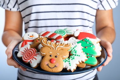 Photo of Woman with plate of delicious gingerbread Christmas cookies on grey background, closeup