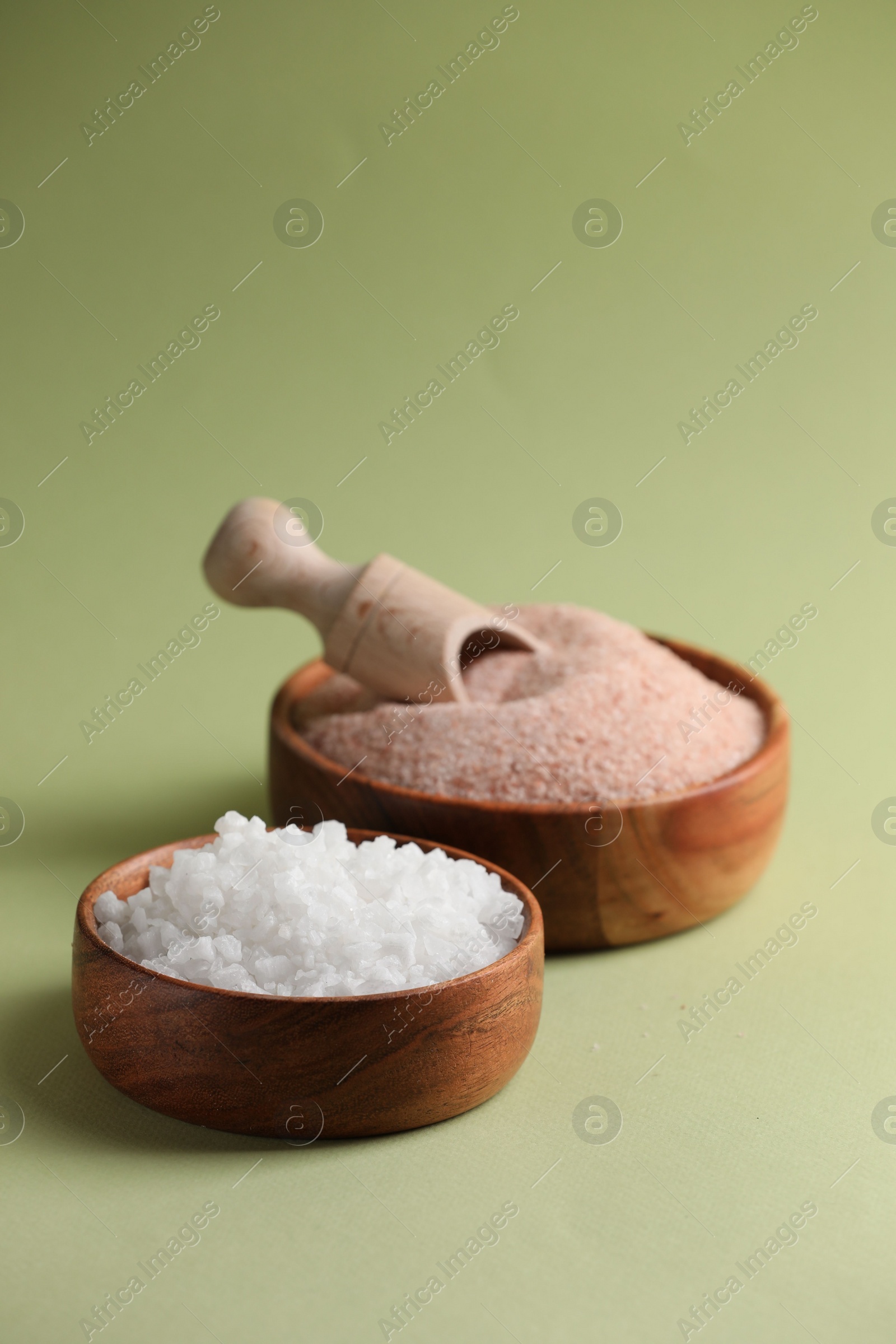 Photo of Different salt in bowls and scoop on green background