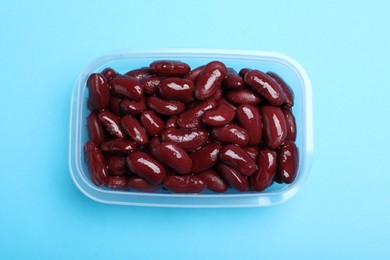 Photo of Fresh red kidney beans in glass container on light blue background, top view