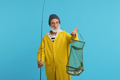 Fisherman holding rod and fishing net with catch on light blue background