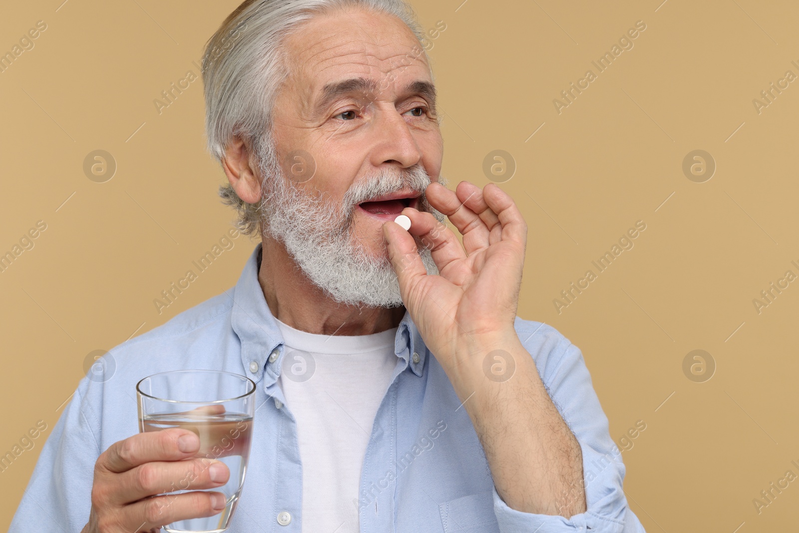 Photo of Senior man with glass of water taking pill on beige background