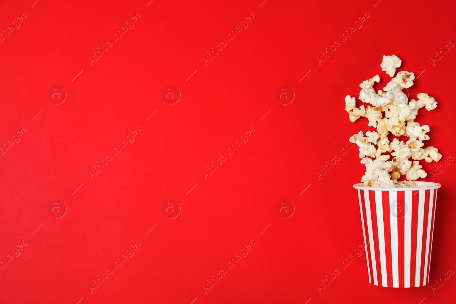 Photo of Overturned paper cup with tasty popcorn on color background, top view. Space for text