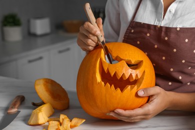 Woman carving pumpkin for Halloween at white marble table in kitchen, closeup. Space for text