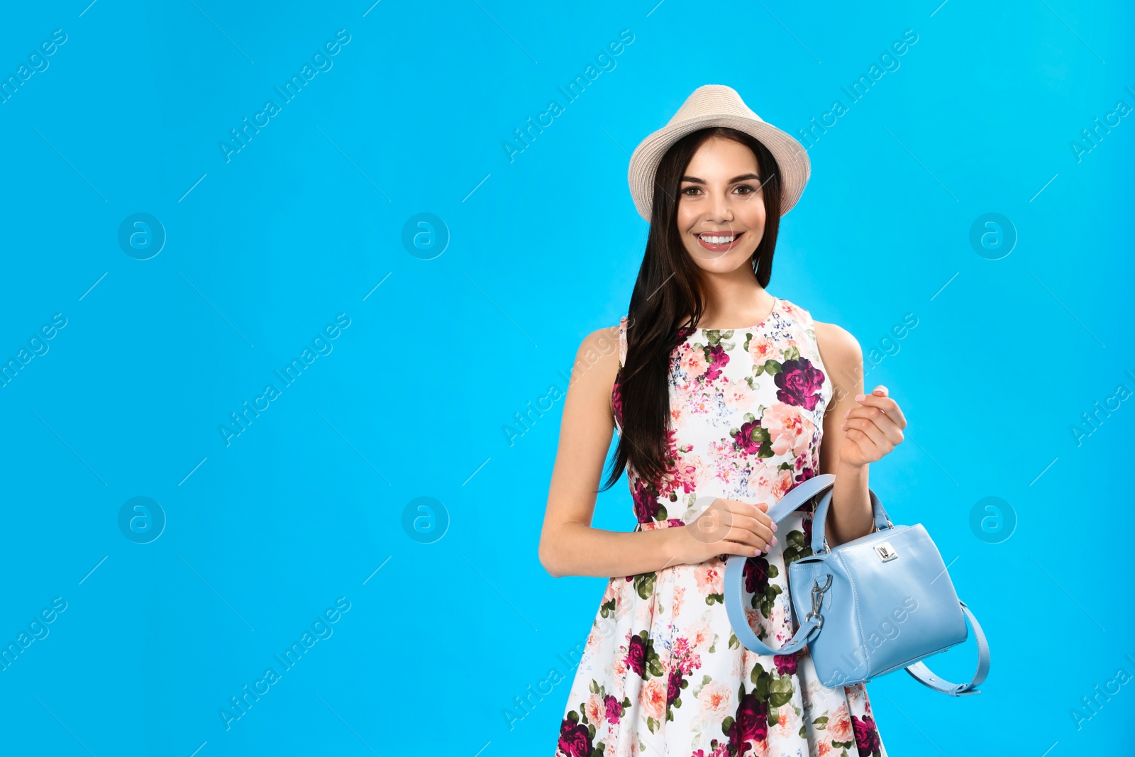 Photo of Young woman wearing floral print dress with stylish handbag on light blue background. Space for text