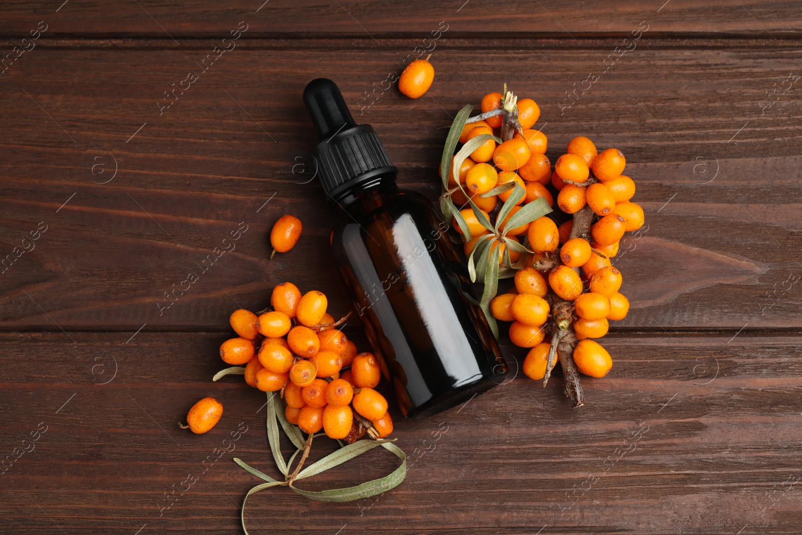 Photo of Natural sea buckthorn oil and fresh berries on wooden table, flat lay