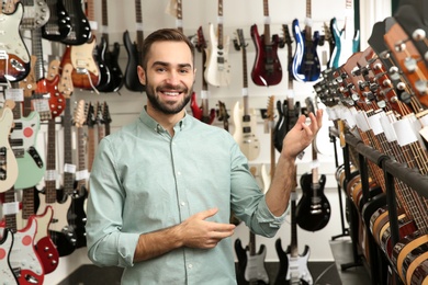 Photo of Young shop assistant near guitars in music store