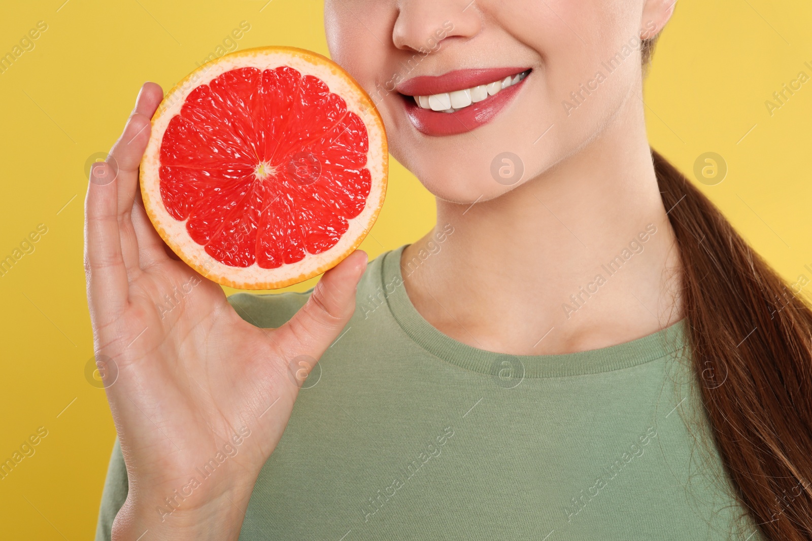 Photo of Young woman with cut grapefruit on yellow background, closeup. Vitamin rich food